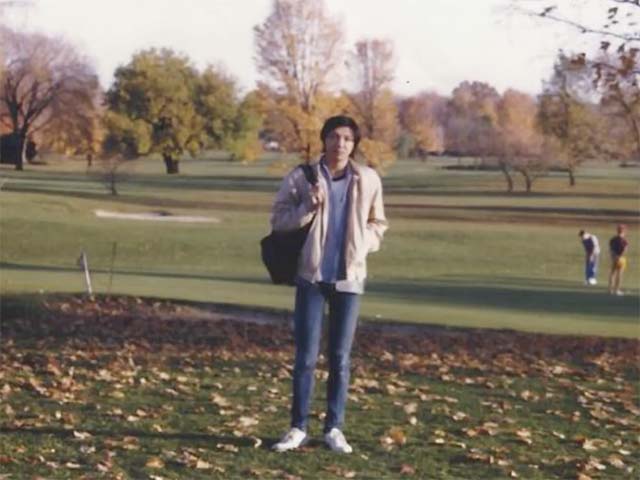 A photo of Xiao as a student holding a backpack and standing near a golf course.